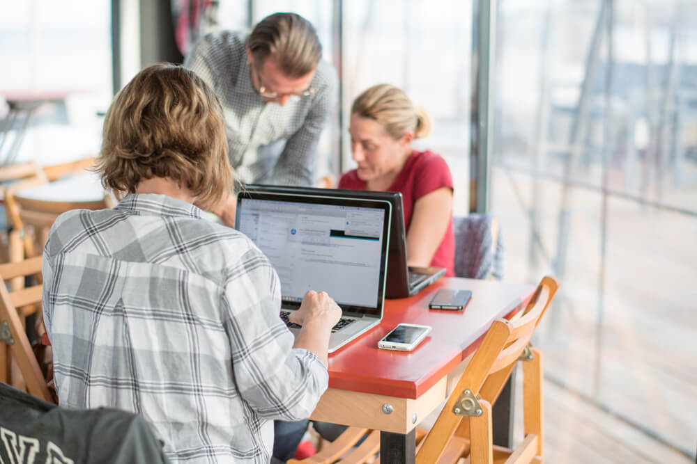 3 adults on table in coffee shop working on laptops