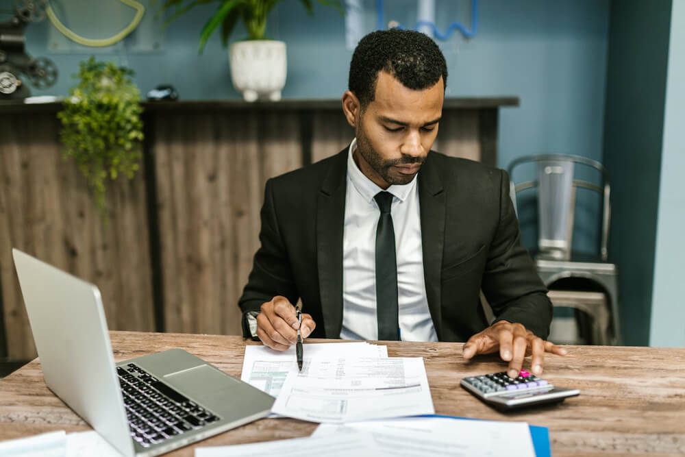 black person in suit analyzing documents with calculator black person in suit analyzing documents with calculator