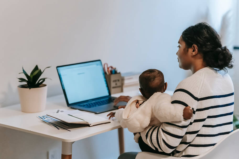black woman with baby on arm filling out tax forms on laptop
